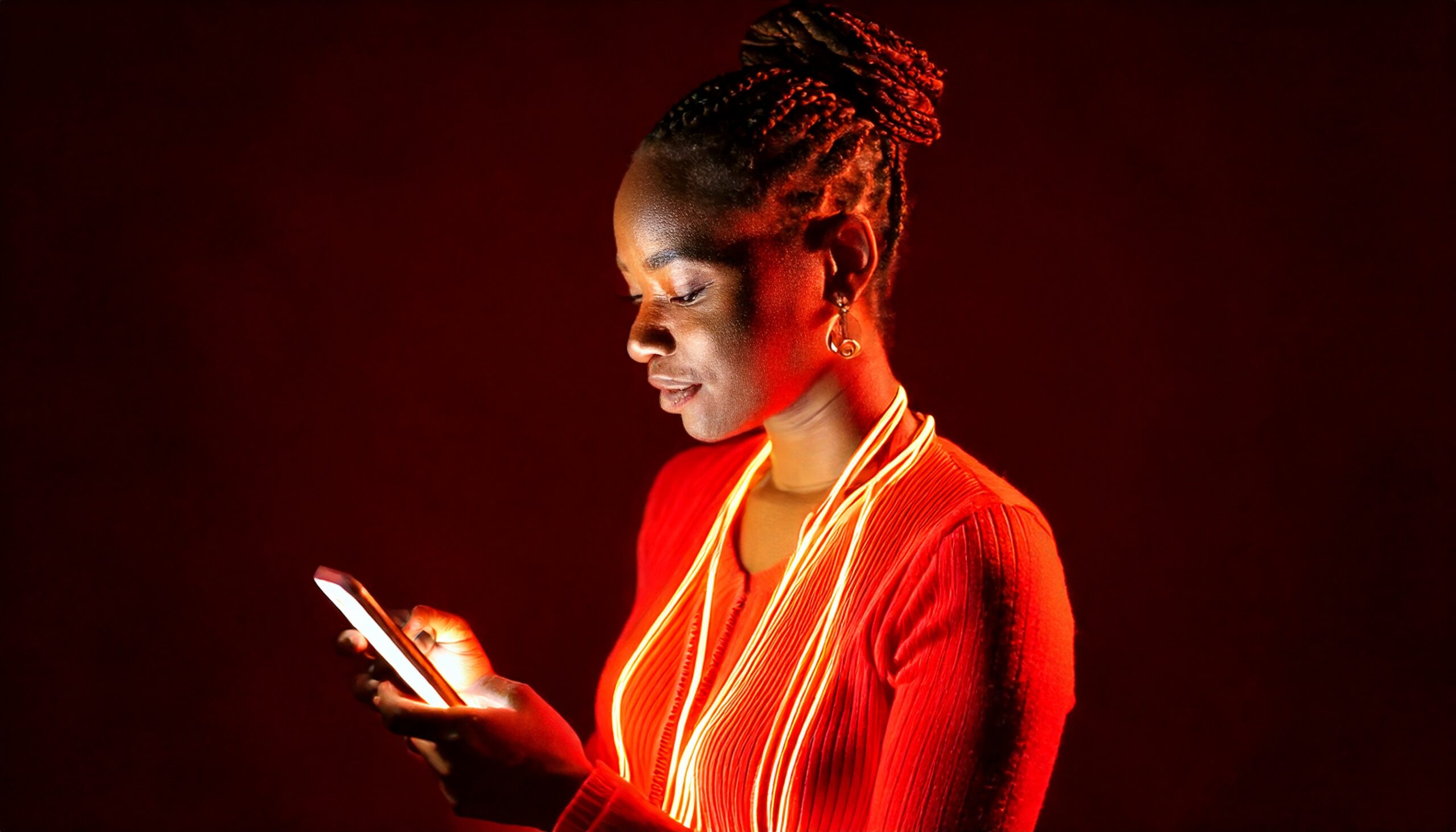 A person looking at their phone. The person is surrounded by neon lights in tones of red