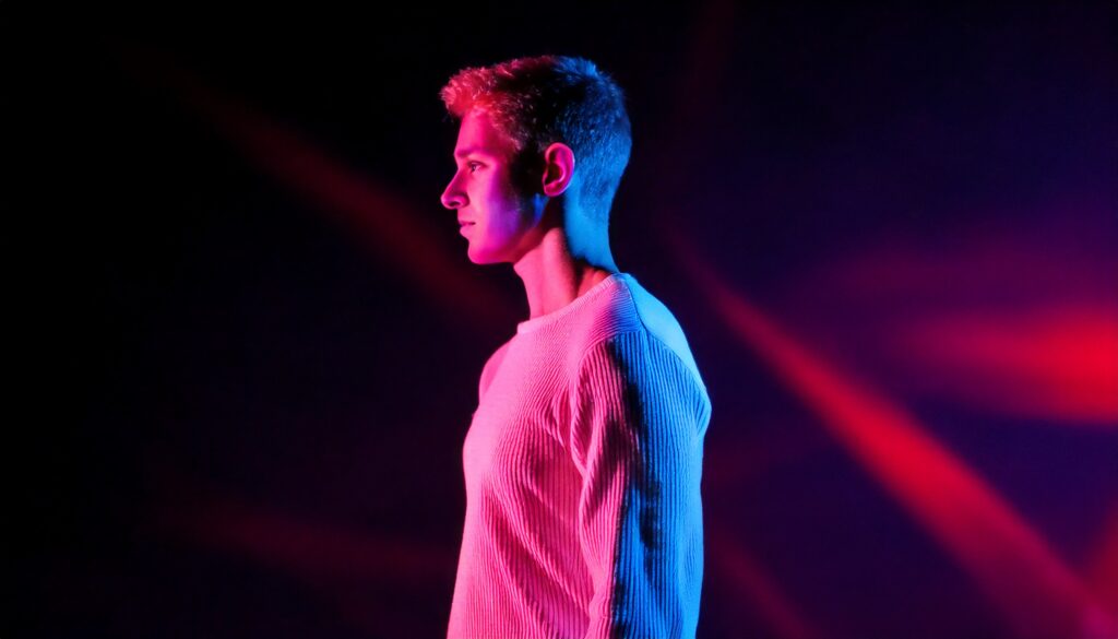 A person looks in the distance. Surrounding him are red and purple lights.