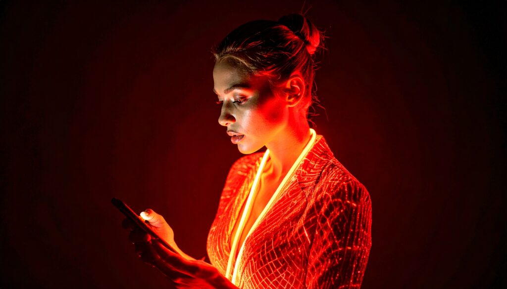 A person looks at her phone. She is surrounded by red neon lights.